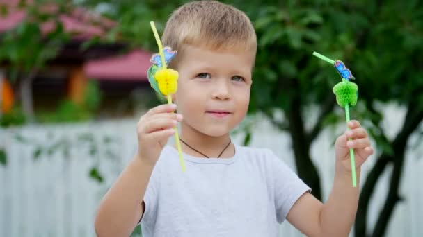 Verano, en el jardín, en cámara lenta, un niño de cuatro años ha decorado la paja para el jugo. Al chico le gustan mucho, se regocija, se divierte, muestra su lengua . — Vídeos de Stock