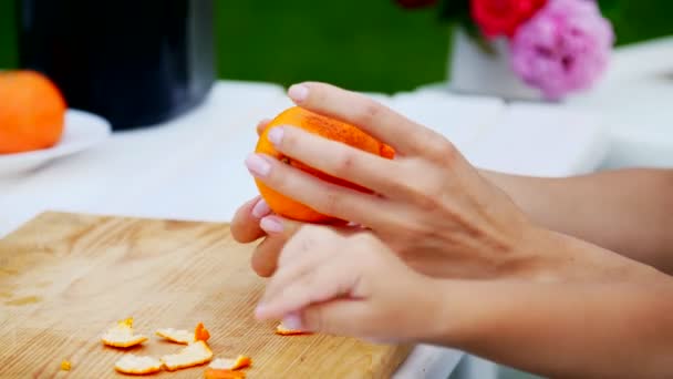 Verano, en el jardín, de cerca, las manos femeninas están pelando una naranja de la cáscara. vacaciones en familia, almuerzo en la naturaleza, en el patio — Vídeo de stock