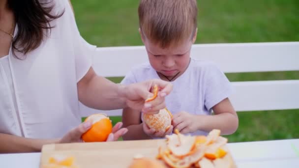 Sommaren i trädgården. Mamma och fyra-årige son rengöras från skala apelsiner. de vill göra färsk juice — Stockvideo