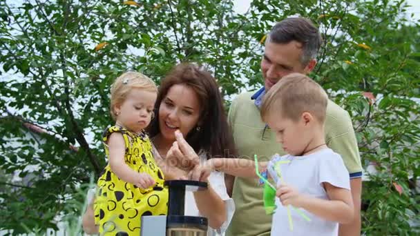 Щаслива красива сім'я, мама, тато, чотирирічний син і однорічна дочка роблять свіжий фруктовий сік. Влітку, в саду. Сім'я проводить дозвілля разом . — стокове відео