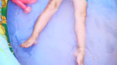 a four-year-old boy lies in a childrens inflatable pool, splashing water, smiling. Nearby float toys. View from above.