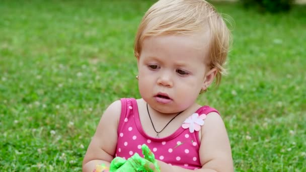 Маленький ребенок, годовалая девочка, играющая, рисующая пальцами, украшающая себя, в саду, сидящая на одеяле, покрывале, на траве, газоне, летом. shes happy fun — стоковое видео