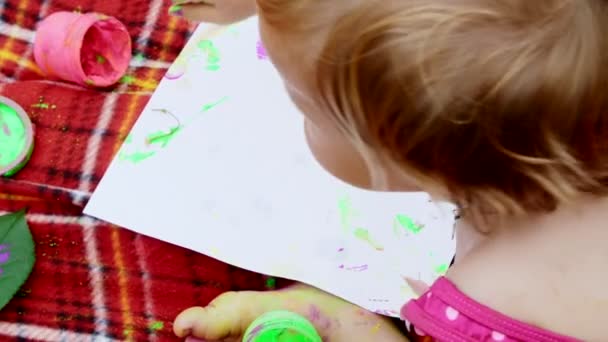 Een kindje, een meisje een-jaar-oude spelen, schilderen met vinger verven, versieren zelf, in de tuin, zittend op een deken, bedspread, op gras, gazon, in de zomer. shes plezier — Stockvideo