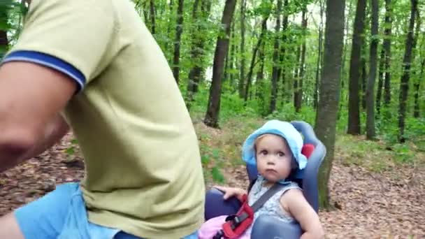 Un hombre con un niño en bicicleta en el bosque, en el verano, el niño está sentado en una silla especial — Vídeos de Stock