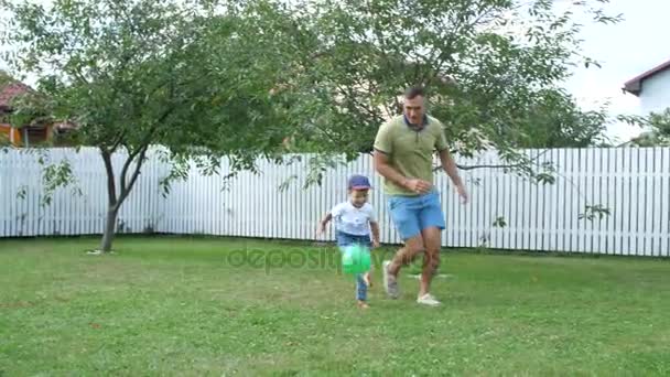 Padre con un hijo de cuatro años jugando pelota, fútbol, en el patio en un césped verde, en el verano . — Vídeos de Stock