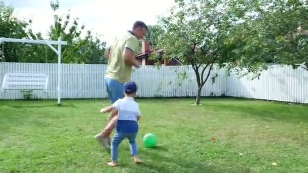 Ο μπαμπάς με ένα τέσσερις-έτος-παλαιό γιο παίζει μπάλα, ποδόσφαιρο, στην αυλή του σε ένα πράσινο γκαζόν, το καλοκαίρι. — Αρχείο Βίντεο