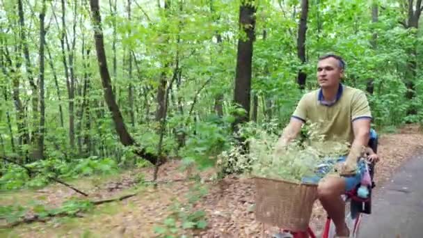 Чоловік з дитиною катається на велосипеді в лісі, влітку дитина сидить в спеціальному кріслі — стокове відео