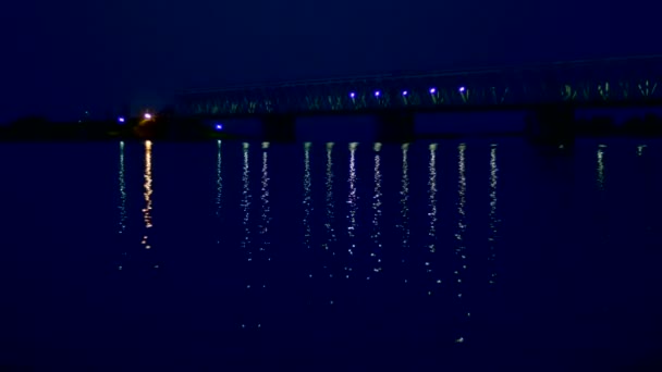 Natten, i vattnet bron och dess ljus reflekteras. En lång bro över floden. — Stockvideo