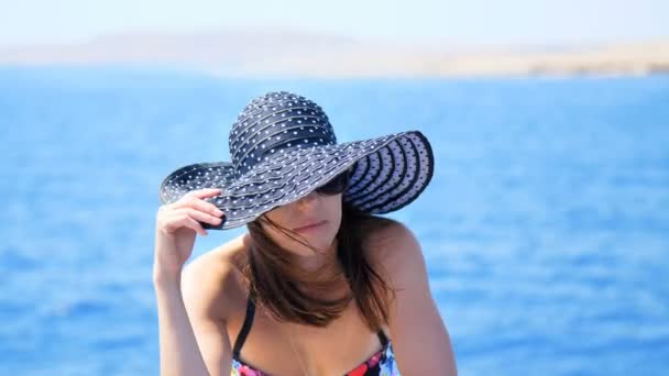 Été, mer, portrait d'une belle jeune femme brune vêtue d'un maillot de bain et d'un chapeau de soleil, lunettes de soleil, debout sur une terrasse de ferry, profitant du repos, beauté de la mer, heureuse, souriante — Video