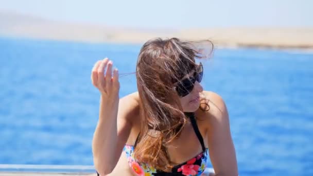 Léto, moře, portrét, krásná mladá bruneta žena na sobě plavky a sluneční brýle, stojící na palubě, užívat si zbytek, její vlasy vlající ve větru, šťastný, — Stock video