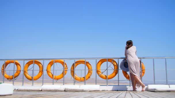Verano, mar, hermosa joven morena, en un vestido largo y gafas de sol, se encuentra en la cubierta de un ferry, barco, disfrutando del resto. a bordo cuelga una gran cantidad de boyas salvavidas . — Vídeos de Stock