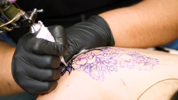 Close-up, in een tattoo salon, een specialist doet een tattoo op dames terug, zwarte verf floral sieraad. een man werkt in de speciale zwarte handschoenen, op speciale apparatuur. — Stockvideo