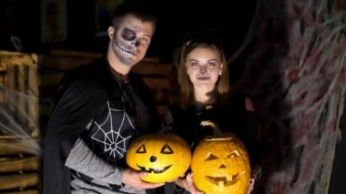 Cadılar Bayramı partisi, gece, ışık, adam kostümler giymiş bir kızla ve korkunç bir makyaj ile ışınları alacakaranlıkta tarzı tarihi olan holding iki büyük Halloween pumpkins