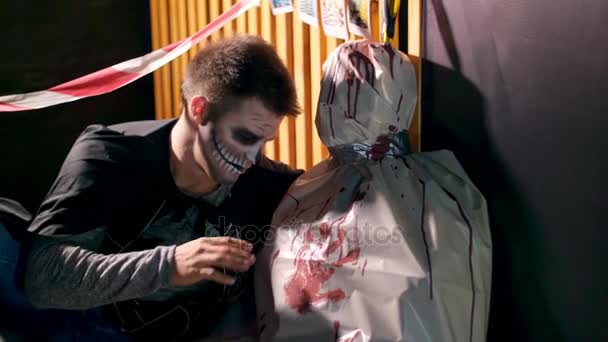 Halloween party, nacht, twilight, in de stralen van licht, een man met een verschrikkelijke make-up praten met een lijk verpakt in wasdoek, het lijk is besmeurd met bloed. — Stockvideo