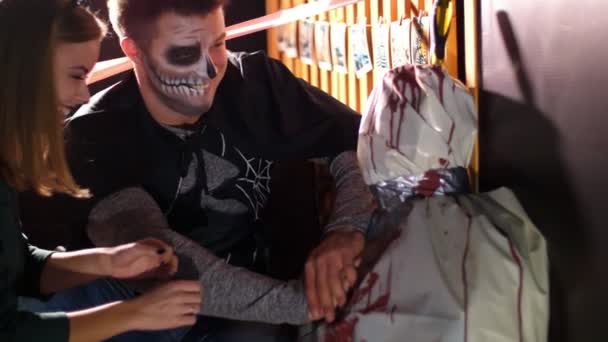 Halloween party, nacht, twilight, in de stralen van licht, een man met een verschrikkelijke make-up en een meisje in een kostuum kat aanbrengt een indirecte hart massage een lijk verpakt in wasdoek, — Stockvideo