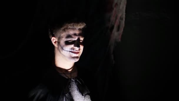 Halloween-Party, Nacht, beängstigendes Porträt eines Mannes in der Dämmerung, in den Lichtstrahlen. Mann mit schrecklichem Make-up im schwarzen Hexenkostüm — Stockvideo