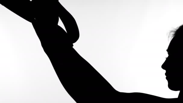 Sobre un fondo blanco, una sombra, un contorno negro de una figura femenina haciendo ejercicios con sistema trx fitness, correas de suspensión TRX . — Vídeo de stock