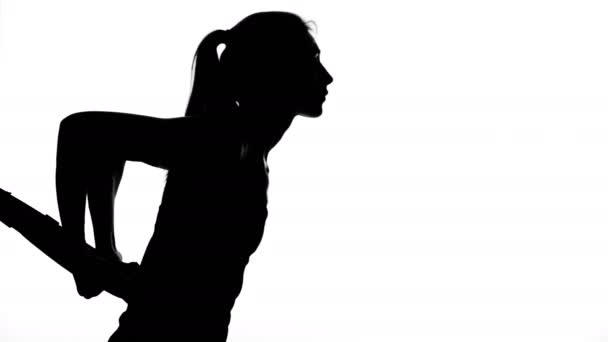 Op een witte achtergrond, een schaduw, een zwarte omtrek van een vrouwelijke figuur doen oefeningen met fitness trx systeem, Trx suspension bandjes. — Stockvideo