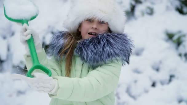 冬の風景の背景に、女の子は雪で庭の楽しみを再生、スロー、シャベルで雪を振りかけます。楽しんで shes. — ストック動画