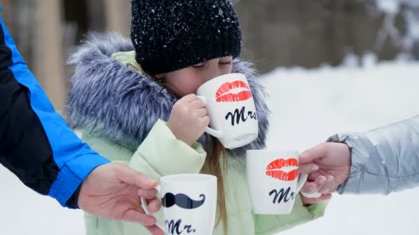 Contra el fondo del bosque de invierno, una niña de siete años bebe té de una taza, en las tazas, se dibujan esponjas. Té familiar en el bosque de invierno, picnic de invierno — Vídeo de stock