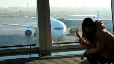 Havaalanında bekleme odasında uçakları ve pist, bakan bir pencere arka planda genç bir kadın onu uçuş için bekleyen oturuyor. Onu siluet görmek