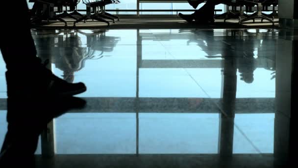 Aéroport, salle d'attente, sur le sol carrelé sont des chiffres reflétés de personnes. Les personnages sombres des gens se pressent d'aller et venir . — Video