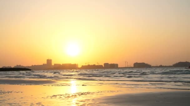 DUBAI, UNITED ARAB EMIRATES, Emirados Árabes Unidos - NOVEMBRO 20, 2017: ao pôr-do-sol, o surf. ondas rolam na areia e se espalham sobre ela. contornos de casas da cidade são visíveis nos raios de luz — Vídeo de Stock