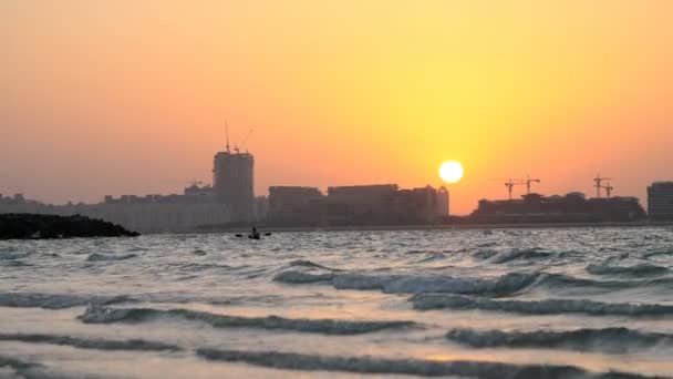 Dubaj, Spojené arabské emiráty, SAE - 20. listopadu 2017: při západu slunce, surfování. vlny najet na písku a rozetřete jej. obrysy domů města jsou viditelné v paprscích světla — Stock video