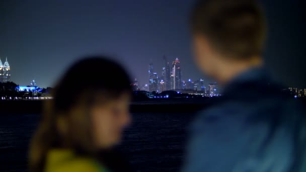 DUBAI, EMIRATOS ÁRABES UNIDOS, EAU - 20 DE NOVIEMBRE DE 2017: noche, en el horizonte, los rascacielos brillan con luces multicolores. contorno borroso de una pareja enamorada admirar la ciudad de la noche — Vídeos de Stock