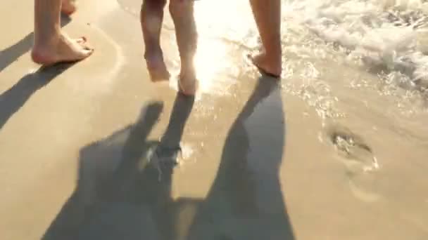 Al tramonto, contro il sole, felice famiglia mamma, papà e bambino. a piedi nudi su sabbia bagnata. surf in mare, primo piano dei piedi. impronte sulla sabbia — Video Stock