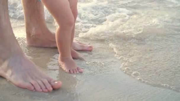 Primo piano, sulla sabbia bagnata, ci sono piedi maschili e per bambini. Arriva un'onda. Vacanze sulla spiaggia dell'oceano, Vacanze estive — Video Stock