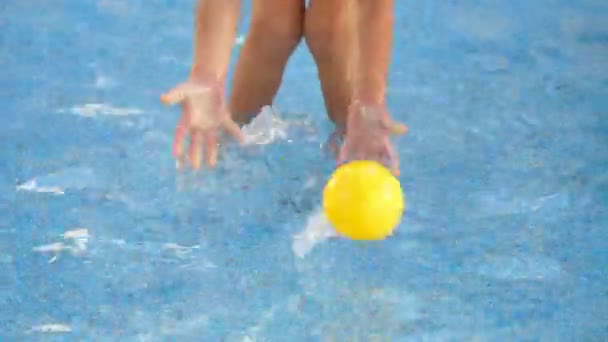 Il bambino gioca con una piccola palla gialla in piscina, la cattura in acqua. Primo piano — Video Stock