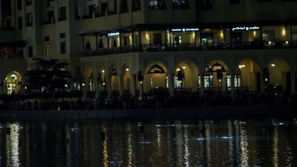 DUBAI, UNITED ARAB EMIRATES, UAE - NOVEMBER 20, 2017: Dancing fountain, beginning of night show, lights flicker on water, restaurant is on background, city lights reflect in water — Stock Video