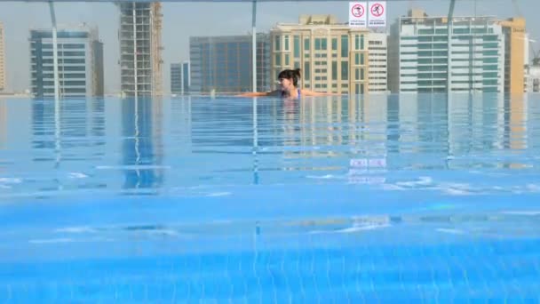 Fille se détendre dans la piscine sur le toit avec vue urbaine sur gratte-ciel — Video