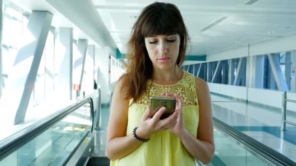 妇女站在自动人行道上, 楼梯在地铁道口, 使用她的手机, 一个沟通的手段, 一个时髦的小玩意。这个概念总是保持联系. — 图库视频影像