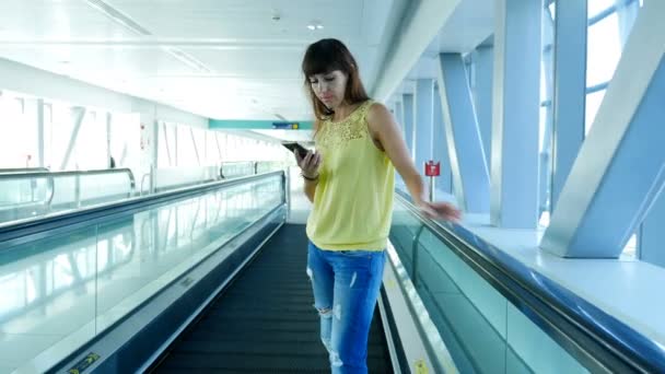 Kvinna som står på automatisk gångväg, trapporna i tunnelbanan passerar, med hennes telefon, ett medelvärde på kommunikation, en fashionabla gadget. Konceptet är alltid i kontakt. — Stockvideo
