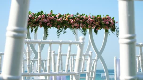 Decoración de la boda, arco de boda blanco decorado con rosas, ceremonia de boda en la playa, preparación para la ceremonia de boda en la playa — Vídeo de stock