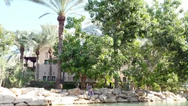 DUBAI, EMIRATOS ÁRABES UNIDOS, Emiratos Árabes Unidos - 20 DE NOVIEMBRE DE 2017: Hotel JUMEIRAH Madinat, a orillas del canal artificial, madre con hija se sienta, admira las bellezas de la naturaleza — Vídeo de stock