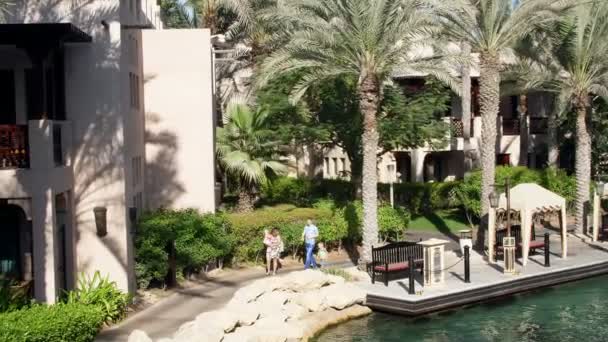 DUBAI, EMIRATOS ÁRABES UNIDOS, Emiratos Árabes Unidos - 20 de noviembre de 2017: Hotel JUMEIRAH DAR AL MASYAF Madinat, paseo familiar matutino por el hotel, todos los verdes están al sol — Vídeo de stock