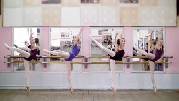 v taneční sál, mladé baletky v purpurové trikotu provádět postoj zahladit na pointe boty, stojící poblíž barre na zrcadla v baletních.