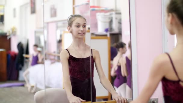 En la sala de baile, Joven bailarina en maillot púrpura realiza el desarrollo a un lado en zapatos de punta, levanta la pierna con elegancia, de pie cerca de la barra en el espejo en la clase de ballet. de cerca — Vídeos de Stock