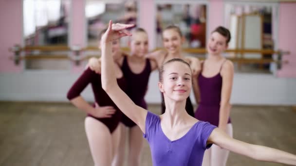 Retrato de una joven bailarina de ballet en un maillot de ballet lila, sonriendo, realizando con gracia una figura de ballet . — Vídeo de stock