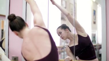 dans salonu, siyah tek parça streç giysi içinde genç balerin gerçekleştirmek yamaç kıstır, zarif eller taşıyarak, barre adlı bale sınıf aynada yakın duran