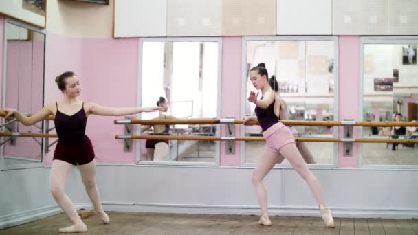 В танцевальном зале, молодые балерины в черных трико растягивают партер, стоят возле барры у зеркала в балетном классе . — стоковое видео