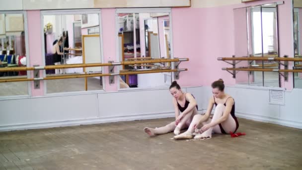 Ballerinas change their shoes into special ballet shoes, pointe shoes, lace with ballet ribbons, on an old wooden floor, in ballet class. — Stock Video