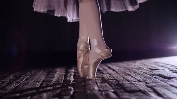 De cerca, en rayos de luz, en el escenario de la antigua sala de teatro. bailarina en falda de ballet blanco, plantea en los dedos de los pies en zapatos de punta, realiza elegantemente un cierto ejercicio de ballet, en tournaht suivi — Vídeo de stock