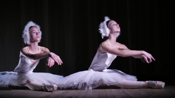 En rayos de luz, en el escenario de la antigua sala de teatro. Bailarinas jóvenes en trajes de cisnes blancos y zapatos puntiagudos, bailan elegantemente cierto movimiento de ballet, parte de sujetadores — Vídeos de Stock