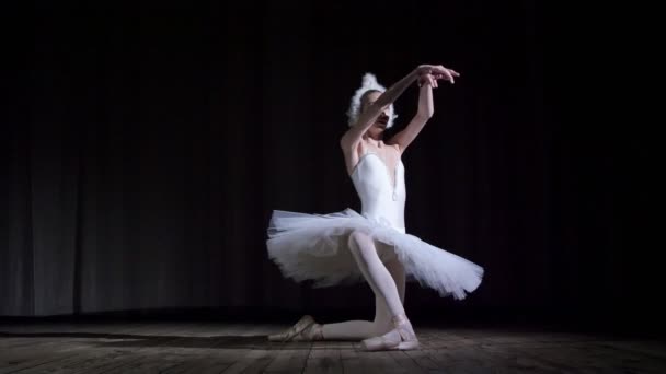 Στις ακτίνες του spotlight, στη σκηνή της αίθουσας παλιό θέατρο. Νέοι μπαλαρίνα στο κοστούμι του λευκού κύκνου και υποδήματα pointe, χορεύει κομψά ορισμένων μπαλέτο κίνηση, bras de μέρος — Αρχείο Βίντεο
