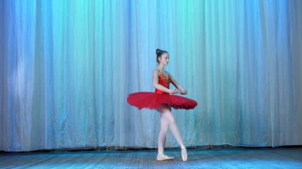 Репетиция балета, на сцене старого театрального зала. Молодая балерина в красных балетных пачках и пуантах, танцует элегантно определенное балетное движение, гастролирует фуитте — стоковое видео
