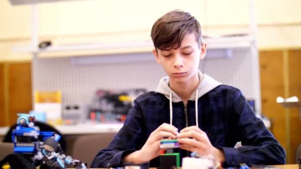Мальчик 12 лет, играет в дизайнере из кубиков, пластин, схем, проводов. маленький изобретатель создает роботов, машины из разных частей дизайнера — стоковое видео